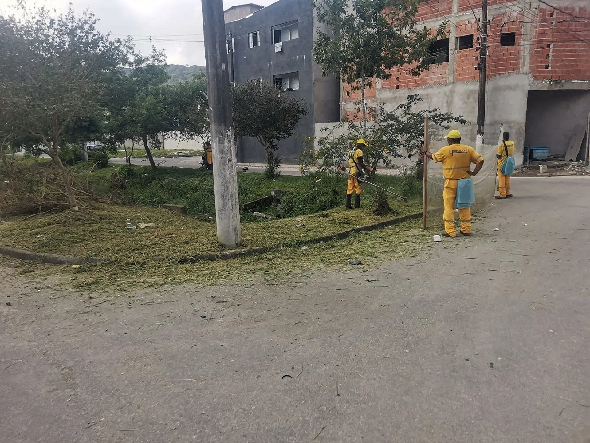 Funcionários uniformizados realizam serviço de roçada em área verde do Victoria Park.